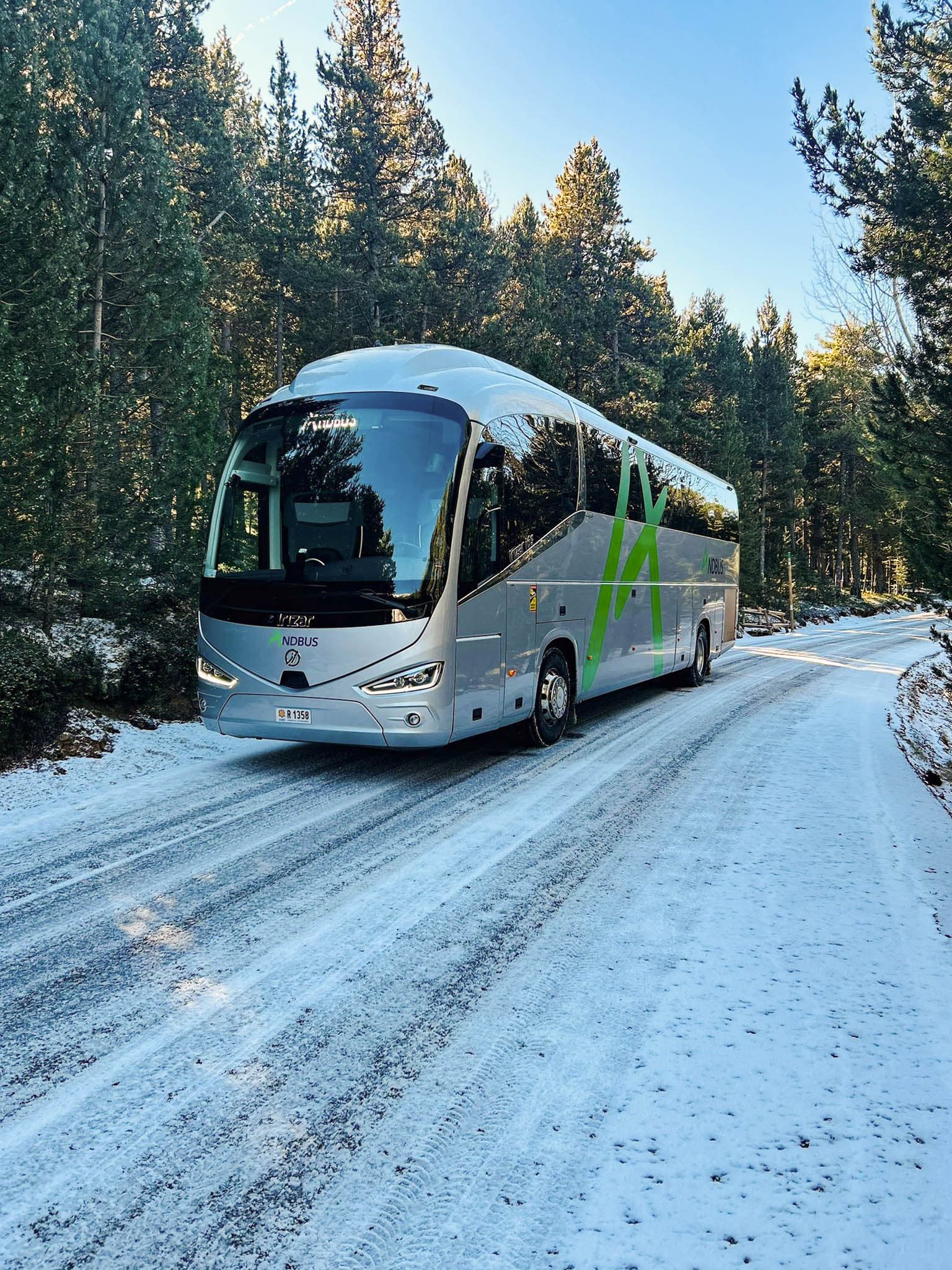 Andbus coach driving through a snowy forest road in Andorra